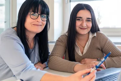 Eine Schülerin und eine Freiwillige sitzen am Tisch mit Lernmaterial