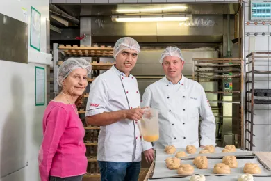 Die freiwillige Mentorin, ein Berufsausbildner und der erwachsene Lernende Hassan stehen in der Bäckerei.