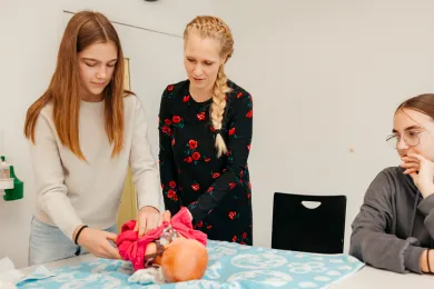 Im Babysitting Kurs SRK üben zwei Teilnehmerinnen an einer Puppe zusammen mit der Kursleiterin das Wickeln.