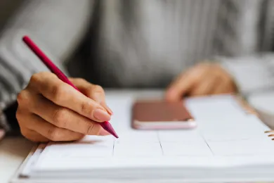 Eine Person macht Notizen, das Handy liegt daneben. 