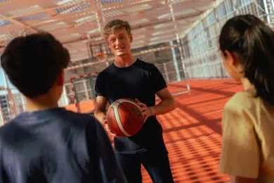 Ein Freiwilliger und zwei Kinder der Ferienwoche spielen gemeinsam Basketball.