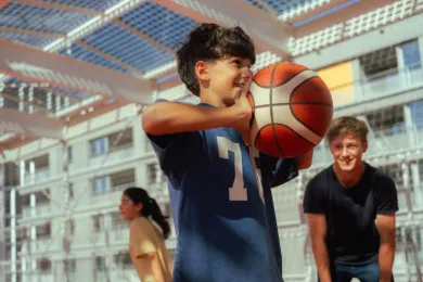 Ein Junge in der Turnhalle spielt mit dem Basketball bei einer JRK-Ferienaktivität