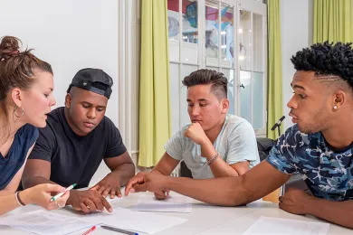 Vier junge Personen unterhalten sich lachend an einem Tisch.