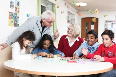 Zwei Freiwillige bringen Kindern bei "mitten unter uns" spielend Deutsch bei.