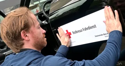 Ein Spieler des EHC Kloten befestigt an seinem Auto das "Rotkreuz-Fahrdienst"-Schild.