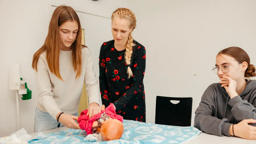 Im Babysitting Kurs SRK üben zwei Teilnehmerinnen an einer Puppe zusammen mit der Kursleiterin das Wickeln.