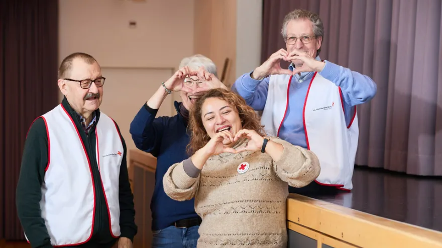 Porträtbild von vier Freiwilligen, die mit der Hand ein Herz formen