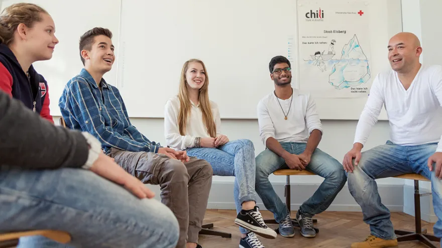 Fünf Personen sitzen im Kreis und sprechen miteinander. 