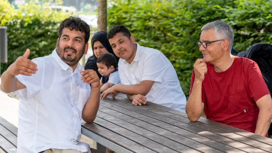 Eine geflüchtete Familie mit Kindern und ein Freiwilliger des Zürcher Roten Kreuzes sitzen in einem Park.