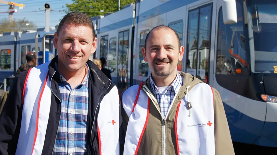 Zwei Geschäftsmänner stehen vor einem Tram und lächeln in die Kamera. 