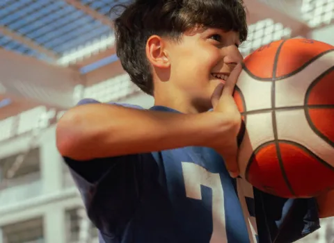 Ein Junge und ein Freiwiliger spielen in der Ferienwoche zusammen Basketball.