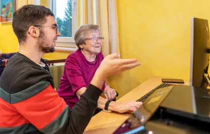 Ein Freiwilliger vom Jugendrotkreuz erklärt einer Bewohnerin etwas am Computer